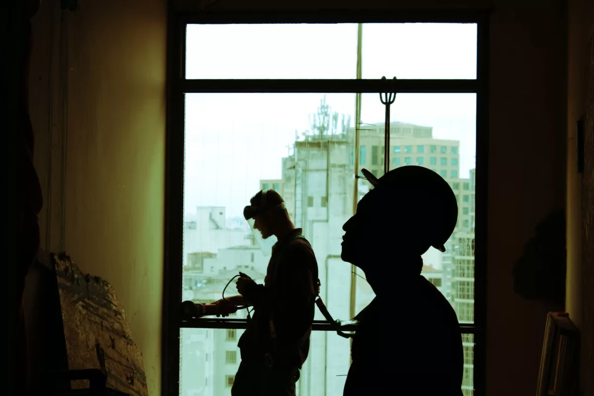 Un hombre con casco, responsable de la durabilidad de las construcciones, se para con confianza frente a una ventana.